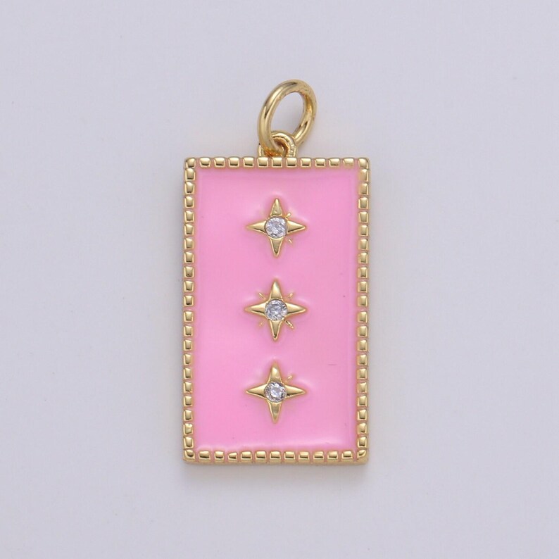 May include: A gold charm with a pink enamel rectangle and three gold stars with clear rhinestones.