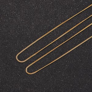 May include: Three gold chains of different lengths on a black background.