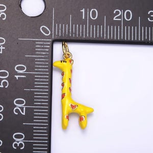 May include: A yellow giraffe charm with red spots and hearts. The charm is about 2 inches tall and is shown next to a ruler.