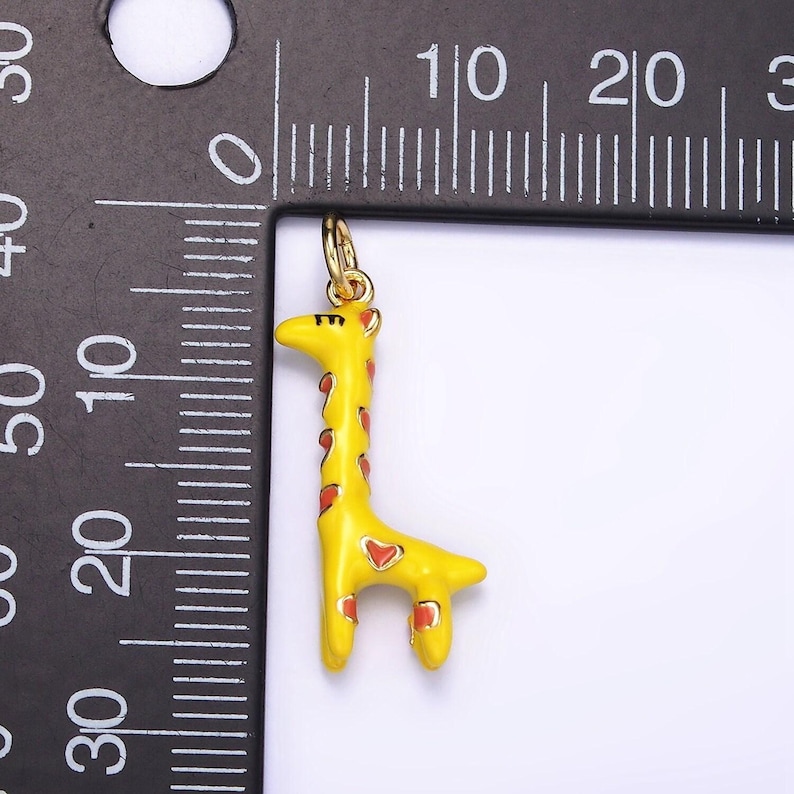 May include: A yellow giraffe charm with red spots and hearts. The charm is about 2 inches tall and is shown next to a ruler.