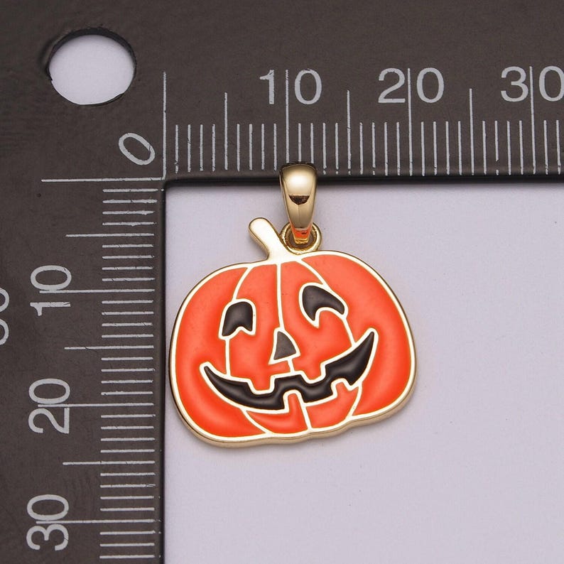 Pu&ograve; includere: Un ciondolo dorato a forma di zucca di Halloween con un viso nero e un corpo arancione.