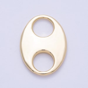 Könnte beinhalten: Ein goldfarbener, oval geformter Anhänger mit zwei kreisförmigen Öffnungen. Der Anhänger hat eine glatte, polierte Oberfläche und ein helles, reflektierendes Finish. Das Design ist schlicht und elegant, geeignet für die Schmuckherstellung.