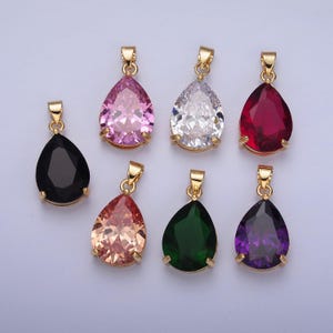 May include: Seven gold teardrop pendants with different colored gemstones. The pendants feature a clear, pink, red, black, peach, green, and purple gemstone.