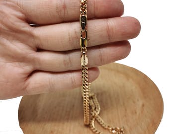 May include: A gold chain necklace with a curb link style. The chain is on a wooden surface.