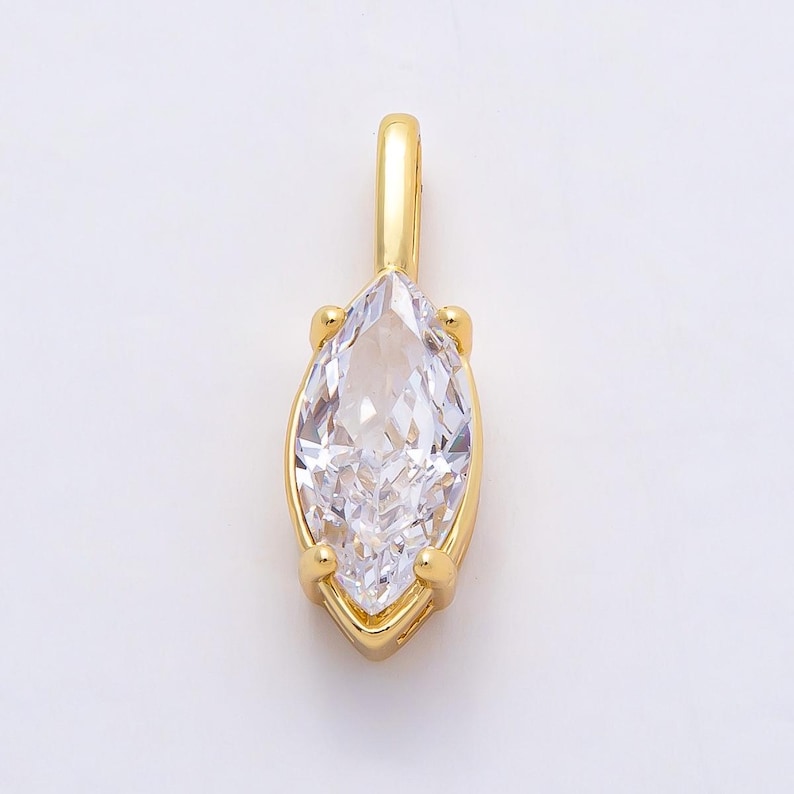 Op de afbeelding: Een goudkleurige hanger met een heldere, marquise-geslepen edelsteen. De edelsteen is gezet in een gouden bezel en heeft een kleine lus voor een ketting. De hanger is ontworpen om als sieraad te worden gedragen.