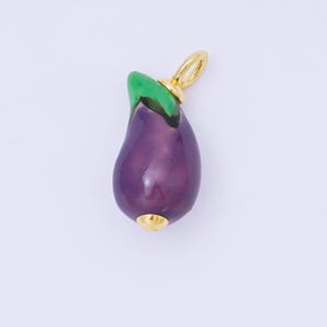 May include: A gold-coloured charm in the shape of an aubergine. The charm has a glossy, deep purple body with a green top and gold accents. The charm is designed with a loop for attaching to a necklace or bracelet.