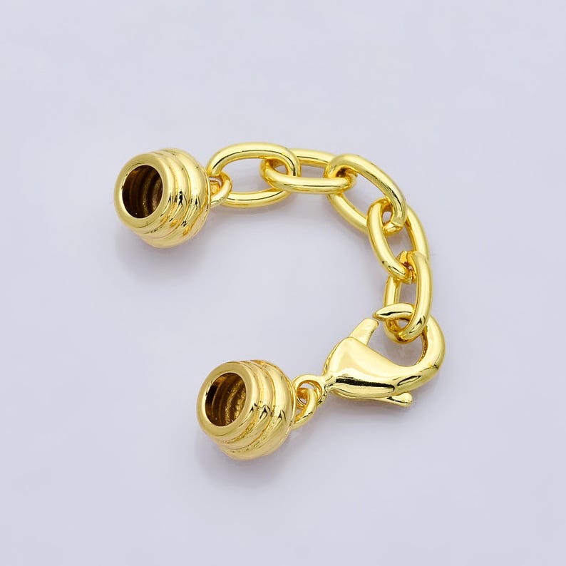 Puede incluir: Un cierre de joyer&iacute;a dorado con una cadena y dos extremos en forma de barril. El cierre tiene un cierre de pinza de langosta y est&aacute; dise&ntilde;ado para conectar piezas de joyer&iacute;a. El metal tiene un acabado brillante.