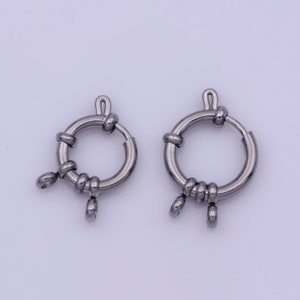 May include: Two silver metal ring clasps with a decorative knot design and three small loops. The clasps are designed for attaching jewelry or other items.