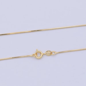 Puede incluir: Un collar de cadena de serpiente de color dorado con cierre de mosquetón. La cadena tiene una superficie lisa y reflectante y un diseño delicado y tejido. El collar se muestra sobre un fondo claro.