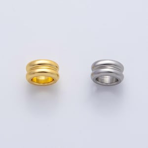 May include: Two metal rings, one gold and one silver, are displayed against a white background. Each ring has a double-banded design. The gold ring has a shiny finish, while the silver ring has a matte appearance. The rings are likely jewelry.