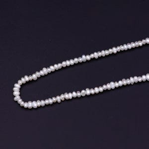 May include: A strand of white freshwater pearls strung on a thin thread. The pearls are small and uniform in size, creating a delicate and elegant look.