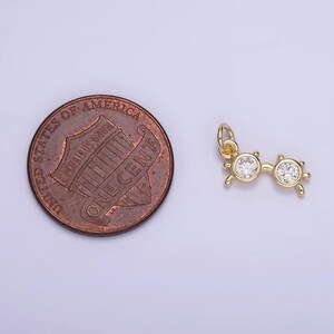 May include: Gold charm in the shape of a pair of sunglasses with clear rhinestones. The charm is about the size of a US penny.