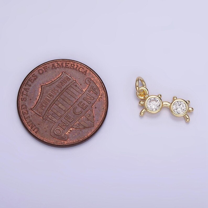 May include: Gold charm in the shape of a pair of sunglasses with clear rhinestones. The charm is about the size of a US penny.