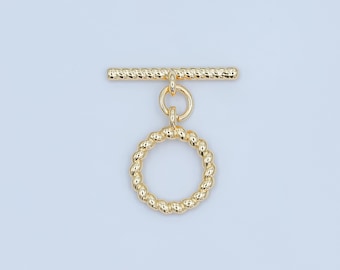 May include: A gold-colored toggle clasp with a textured bar and a circular ring. The ring and bar have a twisted rope design. The clasp is designed for jewelry making and is shown against a light blue background.