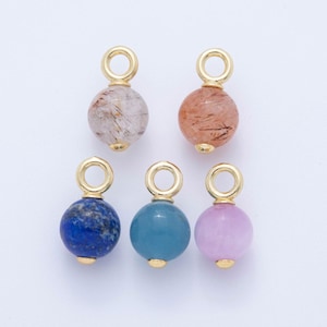 May include: A collection of gemstone pendants with gold-colored findings. The pendants feature round beads in various colors, including clear with brown inclusions, orange, blue, teal, and lavender. Each pendant has a small gold-colored cap and a loop for hanging.