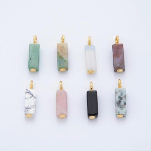 May include: Eight rectangular gemstone pendants with gold-colored metal accents. The pendants vary in color, including green, beige, white, purple, pink, and black. Each pendant has a gold loop at the top for hanging.