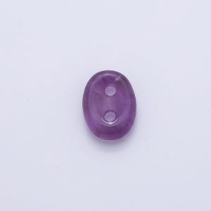 May include: A polished, oval-shaped button in a deep purple hue. The button has two evenly spaced holes and a smooth, glossy surface. The button is likely made of a gemstone or high-quality material.