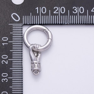 K&ouml;nnte beinhalten: Ein silberfarbener Anh&auml;nger mit einer Hand, die einen Ring h&auml;lt. Die Hand ist detailliert mit geformten Fingern und einer dekorativen Manschette. Der Ring ist an der Hand befestigt und hat einen Verschluss. Der Anh&auml;nger wird neben einem Lineal gezeigt.