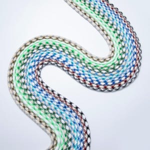 May include: A collection of colorful, patterned cords arranged in a wavy, serpentine design. The cords feature a repeating star-like pattern in various colors, including blue, green, white, and brown. The cords are likely used for crafting or decorative purposes.