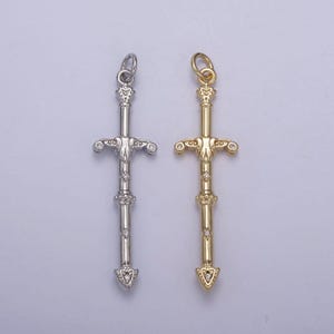 Peut inclure: Deux pendentifs en forme d'épée, l'un en argent et l'autre en or, avec des accents de cristal transparent. Les deux pendentifs ont un design détaillé et une pointe pointue.