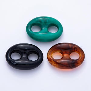 Puede incluir: Tres botones ovalados en tonos verde, negro y marrón. Cada botón tiene dos agujeros y un aspecto veteado. Adecuados para ropa o proyectos de artesanía.