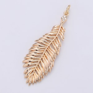 May include: A gold-tone feather charm with clear crystal accents. The feather is detailed with a textured design and has a loop at the top for attaching to a necklace or bracelet.