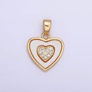 Op de afbeelding: Een gouden hartvormige hanger met een kleiner hartvormig ontwerp in het midden, bezet met heldere zirkonia-stenen.