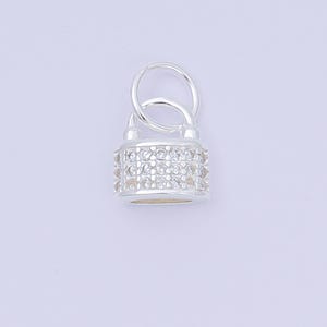 May include: A silver-colored padlock charm with a loop for attaching to a necklace or bracelet. The body of the padlock is encrusted with small, clear crystals, adding sparkle. The charm is designed to be a decorative jewelry element.