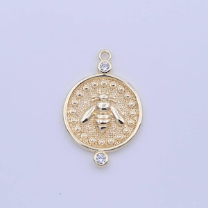 May include: Gold-toned pendant featuring a bee design with clear crystal accents. The pendant is round and has a textured surface.