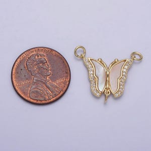 May include: Gold butterfly charm with white mother of pearl wings and clear rhinestones. The charm is about the size of a US penny.