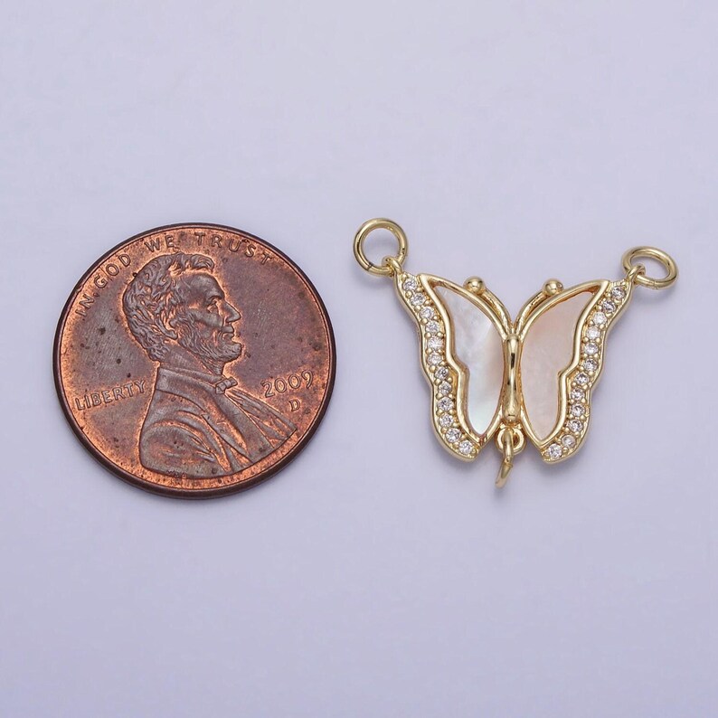 May include: Gold butterfly charm with white mother of pearl wings and clear rhinestones. The charm is about the size of a US penny.