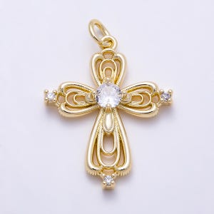 May include: A gold-toned metal cross pendant featuring an intricate openwork filigree design. The center is set with a single round clear gemstone, while smaller clear stones are embedded at the top, bottom, and both side ends of the cross.