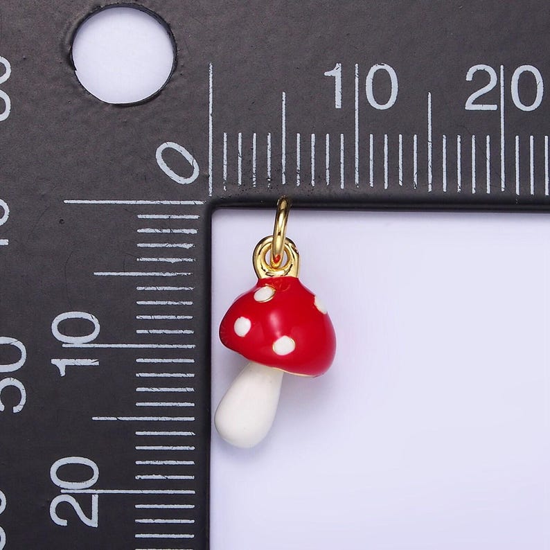 May include: A red and white mushroom charm with white polka dots. The charm is made of metal and has a gold finish. It is about 1 inch tall.