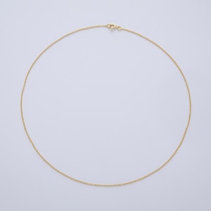 K&ouml;nnte beinhalten: Eine zarte, goldfarbene Halskette mit einem schlichten Kettendesign. Die Halskette wird vor einem schlichten, wei&szlig;en Hintergrund pr&auml;sentiert, der ihren minimalistischen Stil hervorhebt. Der Verschluss ist oben sichtbar.