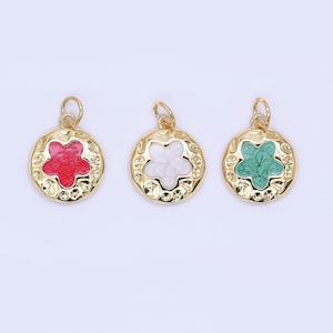 May include: Three gold-colored pendants with a textured border and a flower-shaped center. One pendant has a red center, another has a white center, and the third has a green center. Each pendant has a small loop at the top for attaching to a chain or bracelet.