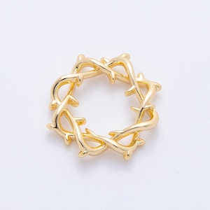 May include: A gold-colored, circular pendant with a thorny design. The pendant is made of a shiny, metallic material and features a detailed, intertwined pattern. The design resembles a crown of thorns.