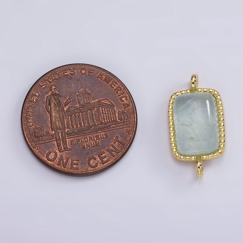 May include: A gold-toned pendant with a light blue gemstone set in a square frame. The pendant has a loop at the top for attaching to a chain.