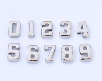 May include: Ten silver metal numbers, from zero to nine, are arranged in two rows against a white background. Each number has a three-dimensional appearance with a shiny, reflective surface. The numbers are evenly spaced and clearly visible.