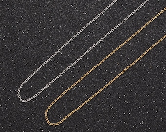 May include: Two chains, one silver and one gold, laid out on a black textured surface. The chains are both delicate and have a simple link design.