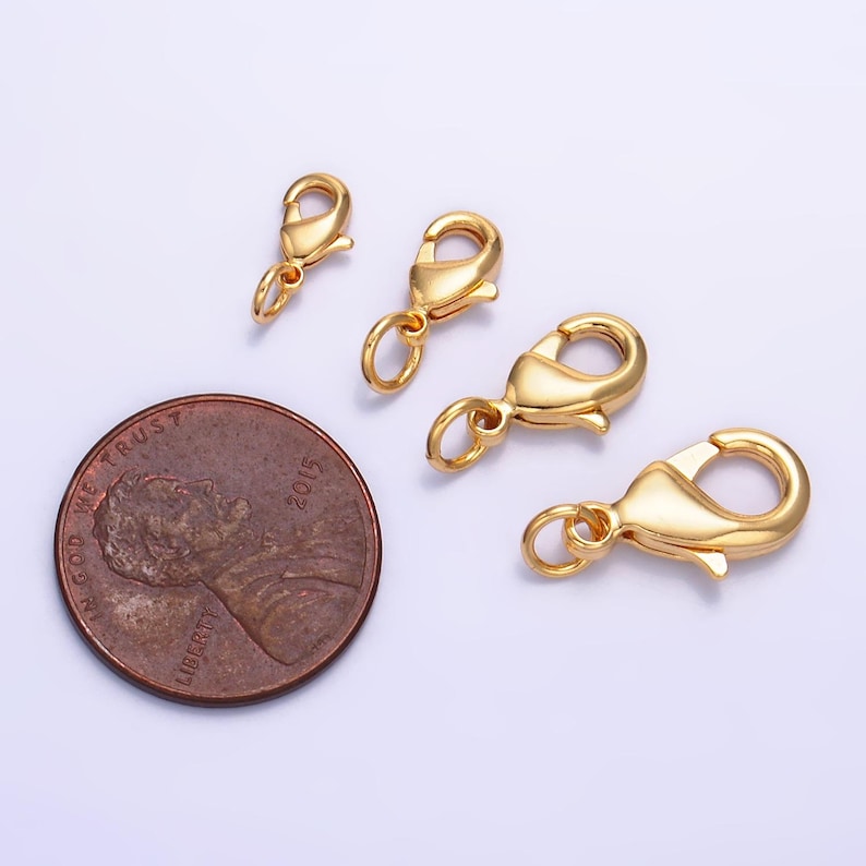 May include: Three gold-toned lobster claw clasps of different sizes. The clasps are shown next to a US penny for scale.
