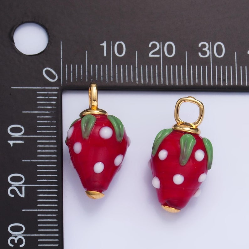 May include: Two red glass strawberry charms with white polka dots and green leaves. Each charm has a gold-colored loop for attaching to jewelry or other crafts.
