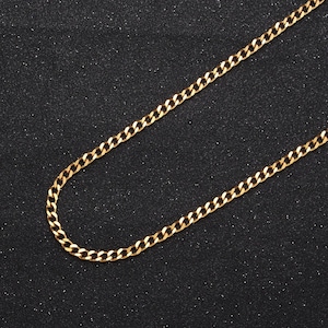 May include: A gold chain necklace with a curb link style. The chain is lying flat on a black surface.