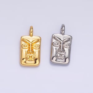 May include: Two pendant charms featuring a stylised face, one in gold and one in silver. Both charms are rectangular in shape and have a detailed face design.