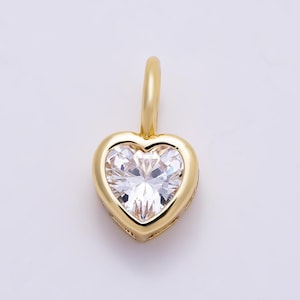 May include: A gold heart-shaped pendant featuring a clear, faceted, heart-cut gemstone set in the center. The pendant includes a smooth, polished gold bail at the top for attachment to a chain, showcasing a clean and reflective metallic finish.