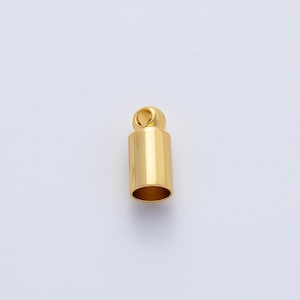 May include: A gold-colored cylindrical jewelry finding with a loop at the top. The finding has a smooth, polished surface and a hollow interior. The jewelry component is designed for use in necklaces, bracelets, or other jewelry projects.