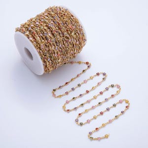 May include: A spool of gold-colored chain with colorful heart-shaped gemstones. The chain is partially unraveled, revealing a delicate strand of the same design. The gemstones are in various colors, including red, pink, yellow, and green.