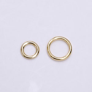 May include: Two gold-coloured metal rings of different sizes are shown against a white background. The rings appear to be made of a shiny, smooth material. The smaller ring is on the left, and the larger ring is on the right.