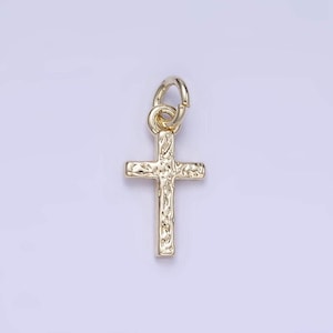 May include: A gold-toned cross charm with a textured surface. The charm has a loop at the top for attaching to a necklace or bracelet.