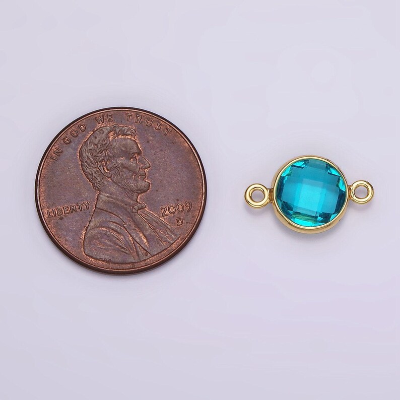 Puede incluir: Conector dorado con una piedra redonda de cristal azul turquesa. El conector es aproximadamente del tama&ntilde;o de una moneda de un centavo de euro.