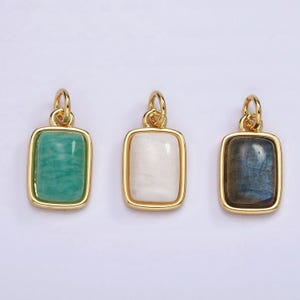 May include: Three gold pendants with different colored stones. The pendants are rectangular with a gold frame and a smooth stone inside. The stones are green, white, and blue.
